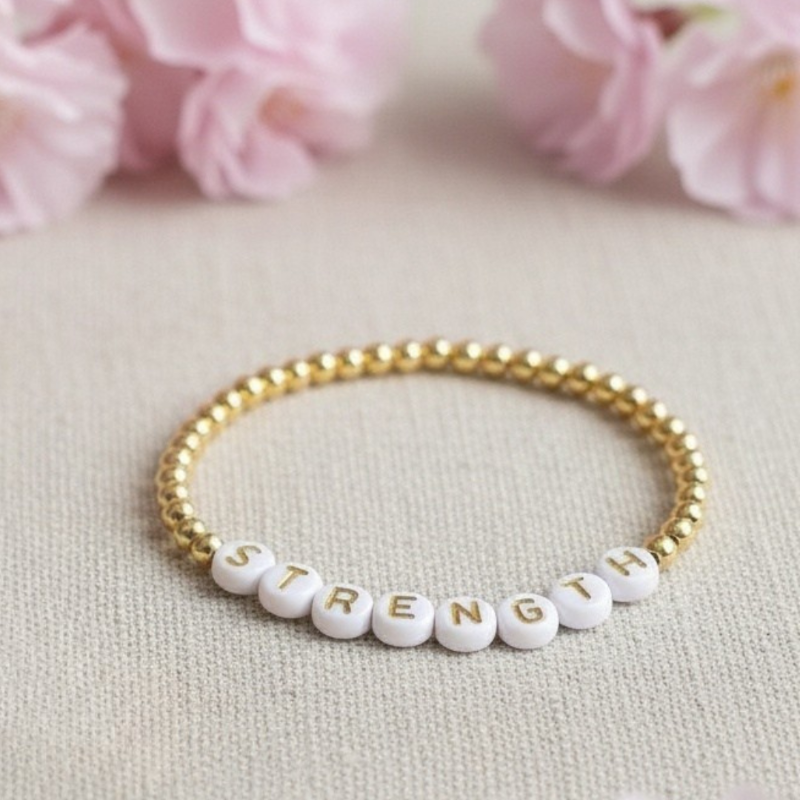 Bracelet with 'STRENGTH' beads on a light background with pink flowers