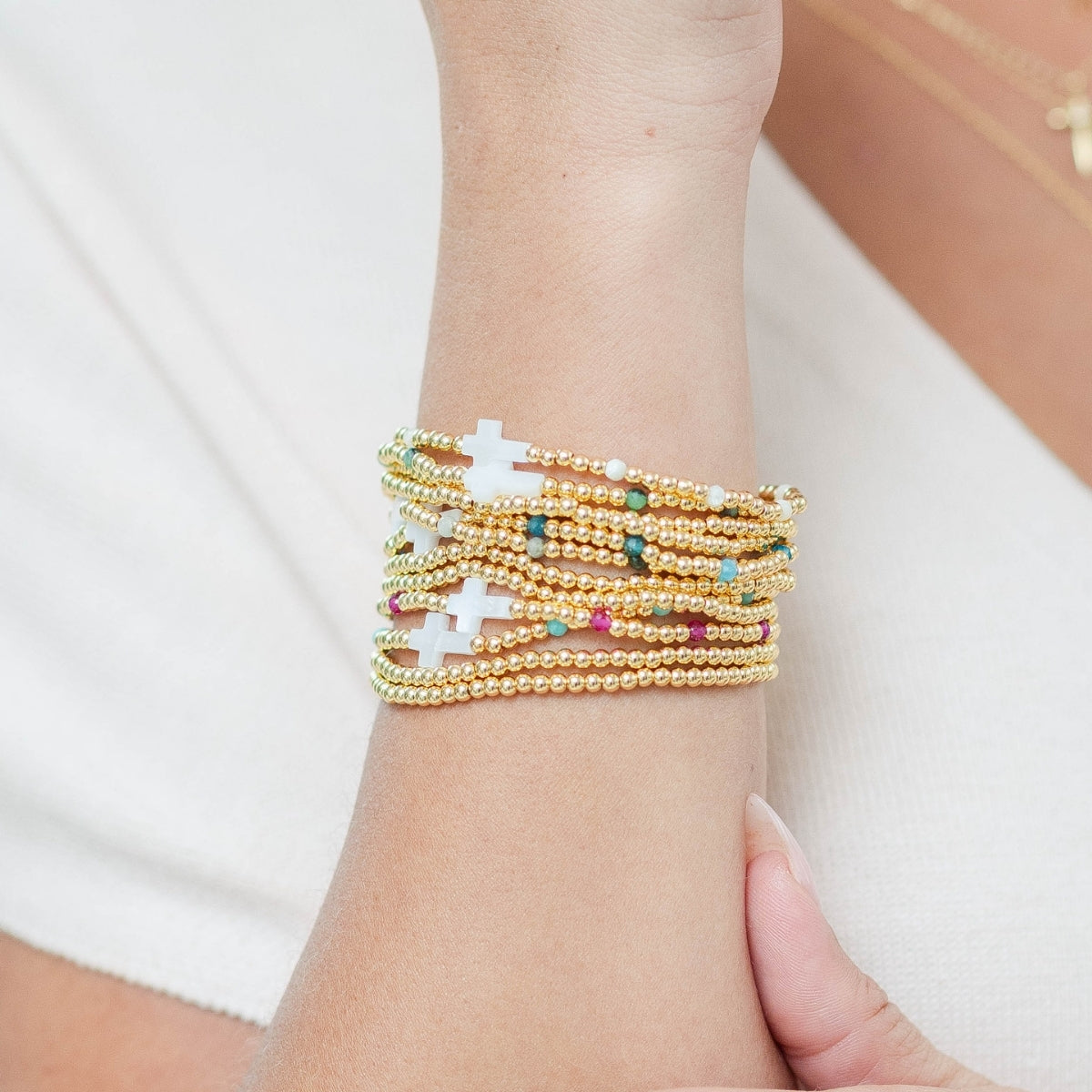 Stack of gold beaded bracelets with cross charms on a wrist against a white background