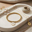 Gold jewelry including a bracelet, necklace, and earrings on a beige surface.