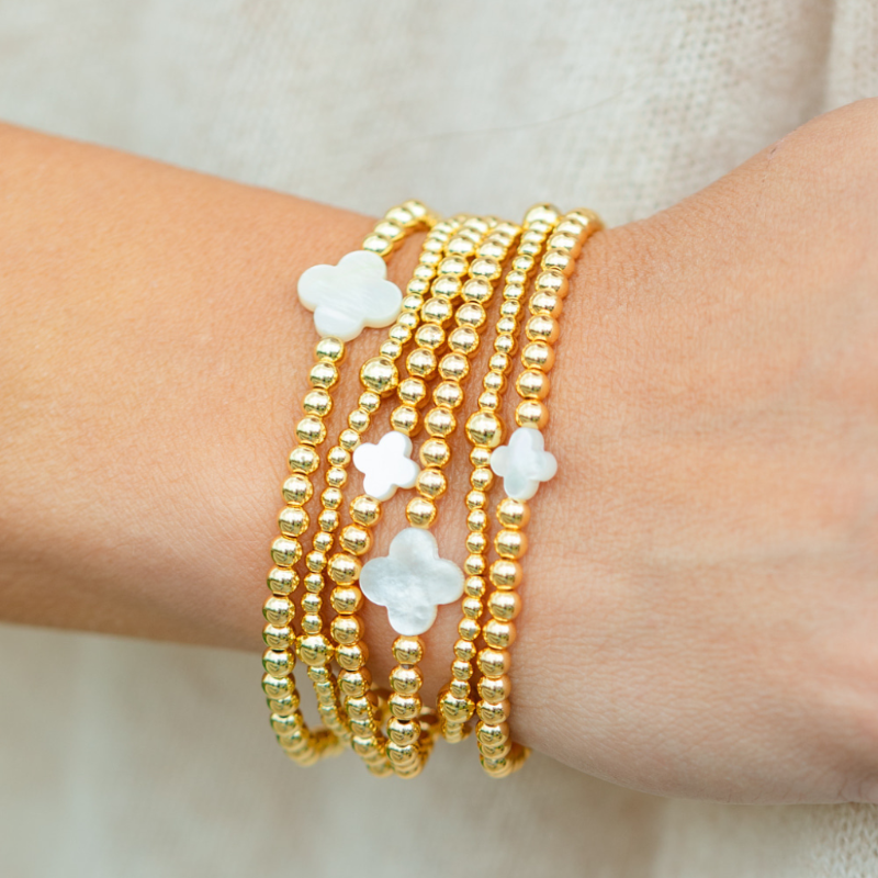 Hand wearing multiple gold bracelets with floral designs on a neutral background