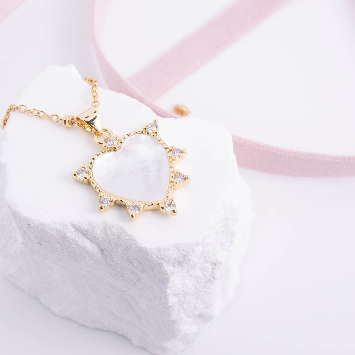Gold heart-shaped necklace with clear stones on a white and pink fabric background