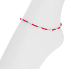 A delicate beaded anklet or bracelet in pink, red, and light blue, displayed on a white mannequin leg against a white background.