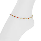 A delicate beaded anklet with small multicolor beads and a central silver-toned charm, displayed on a white mannequin foot against a white background.