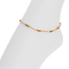 A delicate beaded ankle bracelet with peach, green, and red beads displayed on a white mannequin leg against a white background.