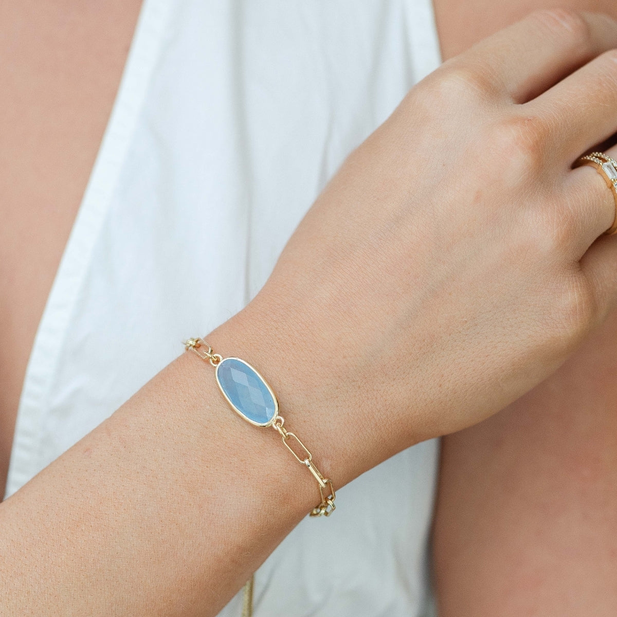 Gold bracelet with a blue stone on a wrist against a white background