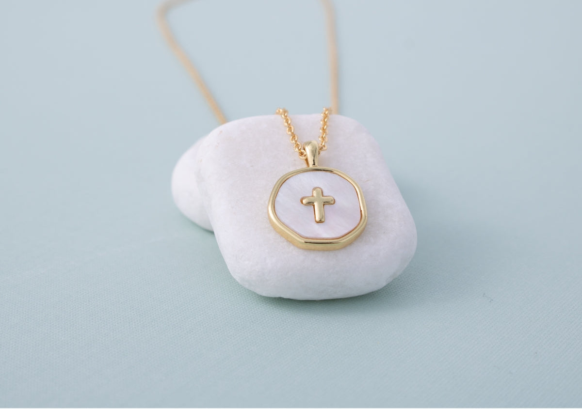 Gold necklace with a cross pendant on a white stone surface