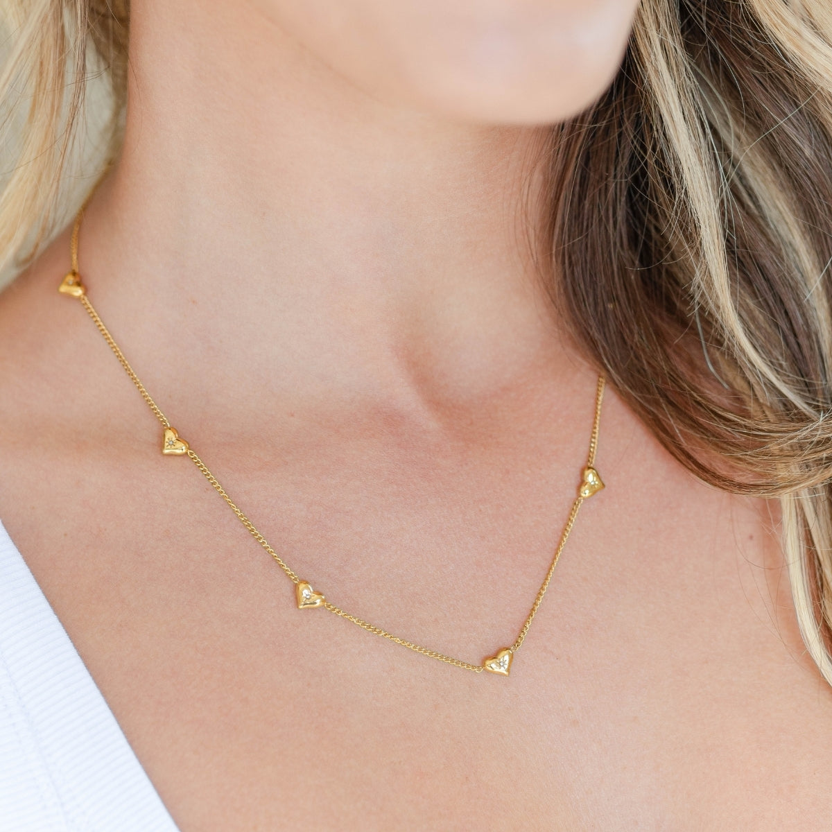 Gold necklace with heart-shaped pendants on a person wearing a white top