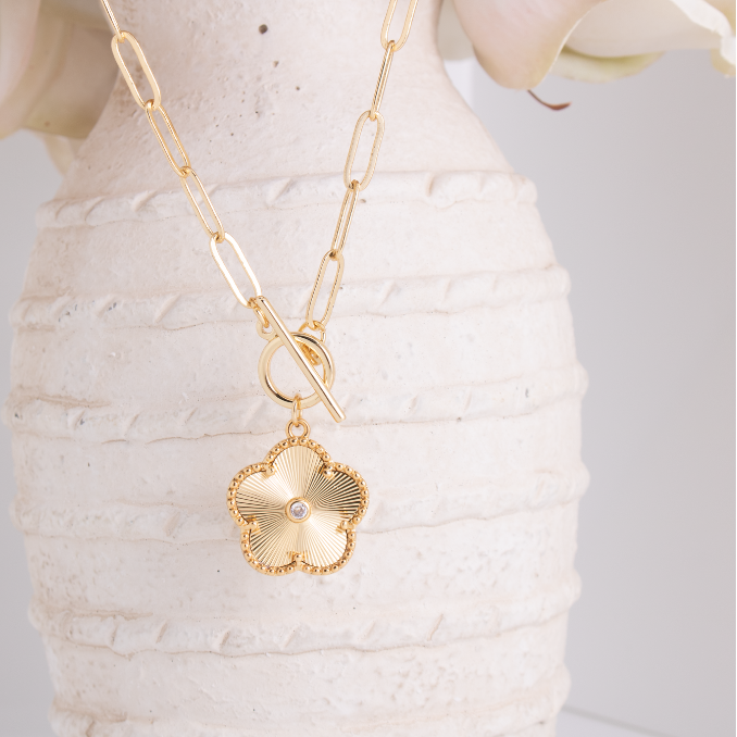 Gold necklace with a floral pendant on a textured white surface